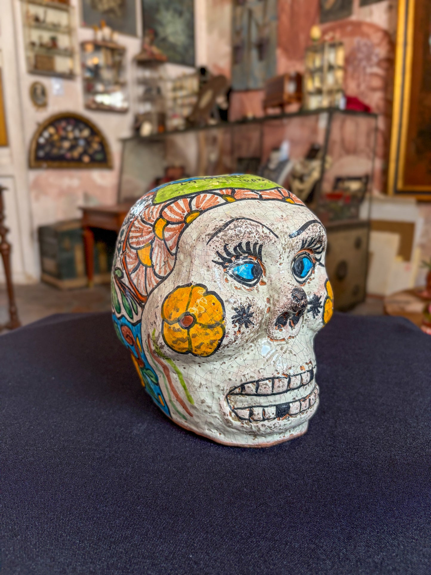 Handcrafted glazed clay skull ornament, Puebla Mexican folk art, three-quarter front, blue eyes and cheek flower